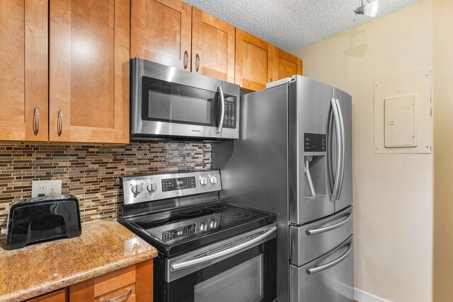 kitchen with a textured ceiling, electric panel, light stone counters, stainless steel appliances, and decorative backsplash