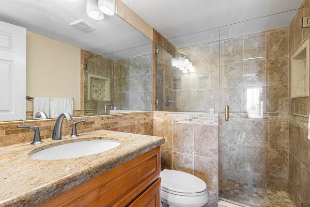 bathroom with tile walls, toilet, vanity, and an enclosed shower