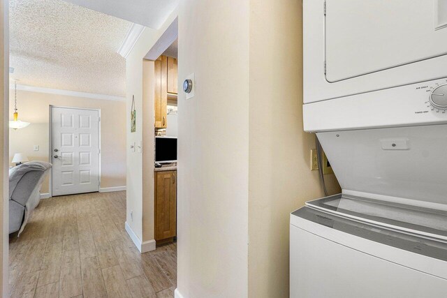 laundry room with stacked washer and dryer, light hardwood / wood-style flooring, a textured ceiling, and ornamental molding