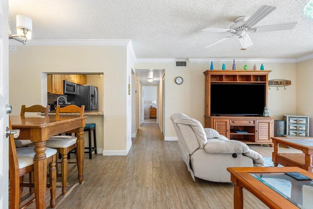 living room featuring light wood-type flooring, ceiling fan, ornamental molding, and a textured ceiling