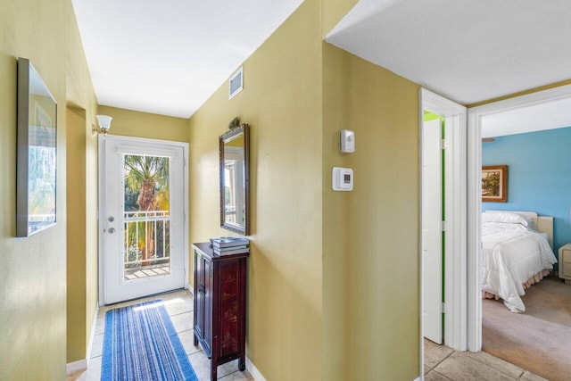 corridor with light tile patterned floors, baseboards, visible vents, and light colored carpet