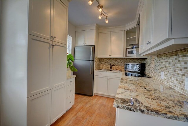 kitchen with light wood-style flooring, a sink, light stone counters, backsplash, and freestanding refrigerator