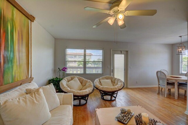 living room with baseboards, light wood-style flooring, and ceiling fan with notable chandelier