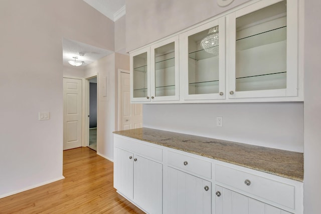 kitchen with light stone counters, glass insert cabinets, light wood-style floors, ornamental molding, and white cabinets