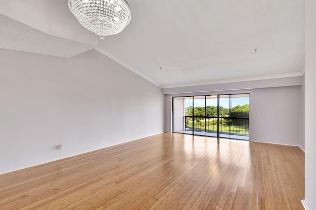 spare room with vaulted ceiling, ornamental molding, light wood-type flooring, and an inviting chandelier