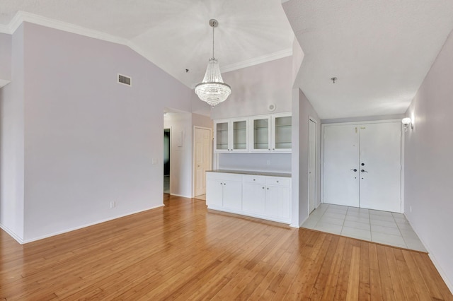 unfurnished living room featuring visible vents, ornamental molding, an inviting chandelier, vaulted ceiling, and light wood-type flooring