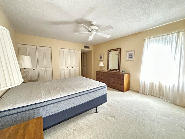 bedroom featuring light colored carpet, multiple closets, a textured ceiling, and ceiling fan