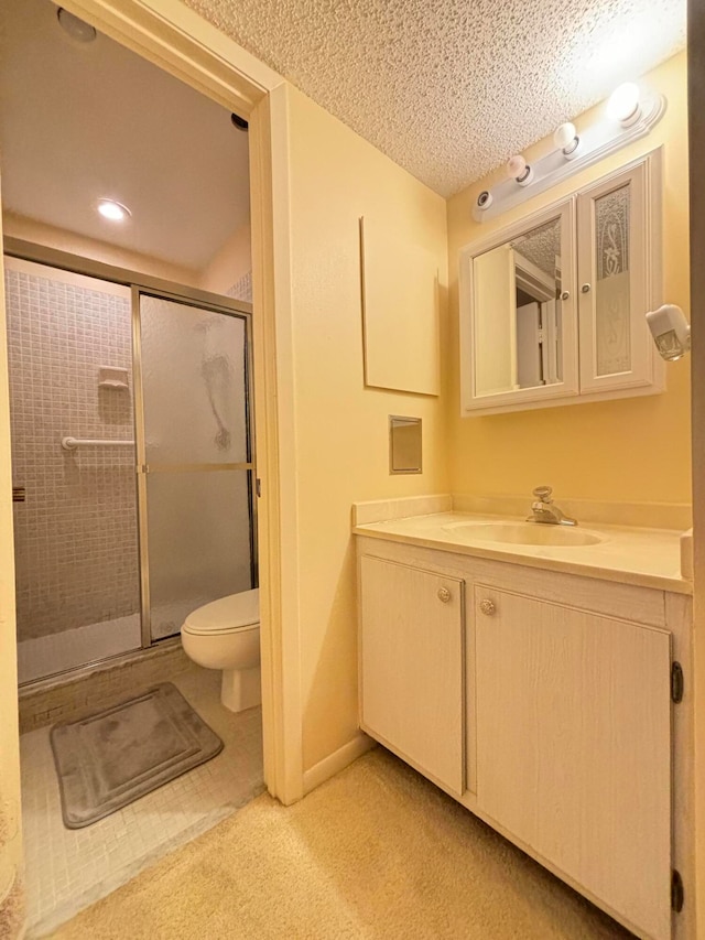 bathroom with vanity, toilet, a shower with door, and a textured ceiling