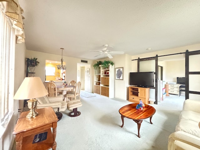 carpeted living room with a textured ceiling, ceiling fan with notable chandelier, and a barn door