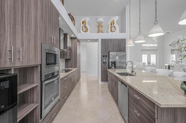 kitchen with appliances with stainless steel finishes, pendant lighting, sink, wall chimney range hood, and a center island with sink