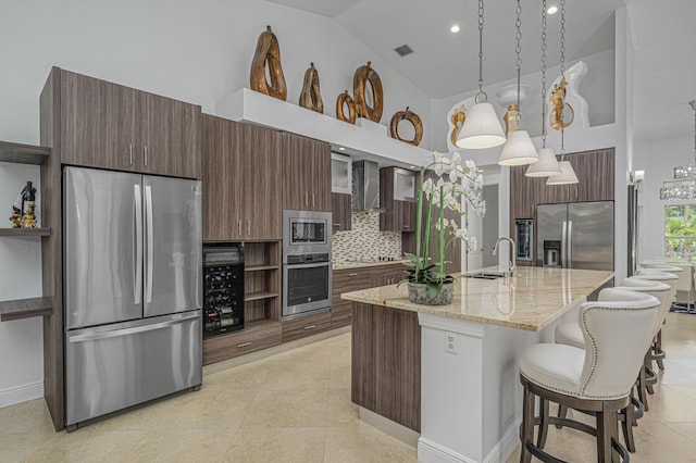 kitchen with a kitchen island with sink, stainless steel appliances, light stone counters, decorative light fixtures, and decorative backsplash