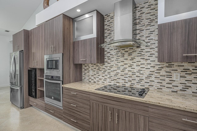 kitchen with vaulted ceiling, wall chimney exhaust hood, tasteful backsplash, light stone counters, and stainless steel appliances