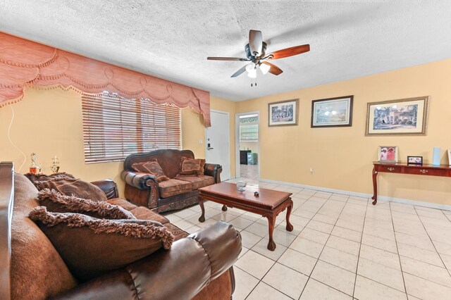 living area featuring a ceiling fan, a textured ceiling, baseboards, and light tile patterned floors