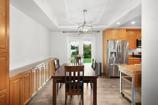 dining room with a raised ceiling, a chandelier, and light hardwood / wood-style floors