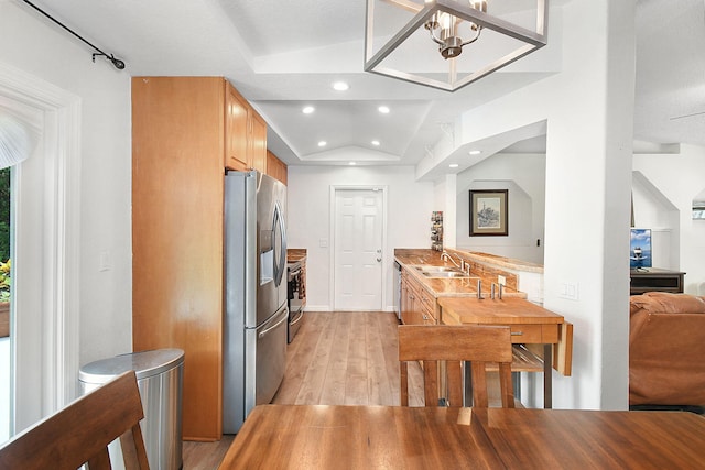 kitchen featuring a notable chandelier, appliances with stainless steel finishes, sink, lofted ceiling, and light wood-type flooring