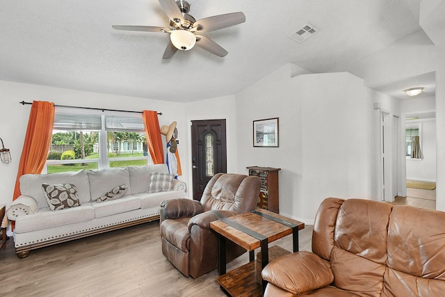 living room featuring lofted ceiling, ceiling fan, light hardwood / wood-style floors, and a textured ceiling