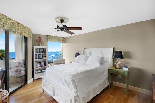 bedroom with multiple windows, ceiling fan, light hardwood / wood-style flooring, and a water view