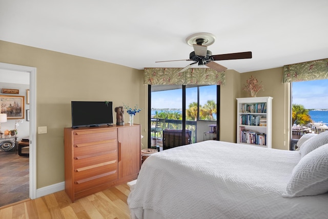 bedroom with access to outside, ceiling fan, hardwood / wood-style floors, and a water view