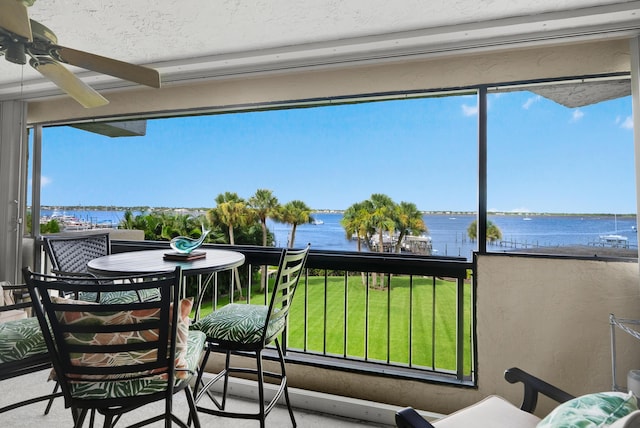 sunroom with ceiling fan and a water view