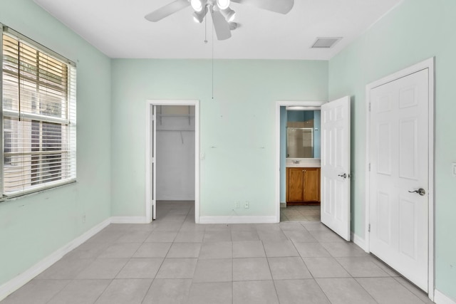 unfurnished bedroom with a spacious closet, light tile patterned floors, ceiling fan, ensuite bath, and a closet