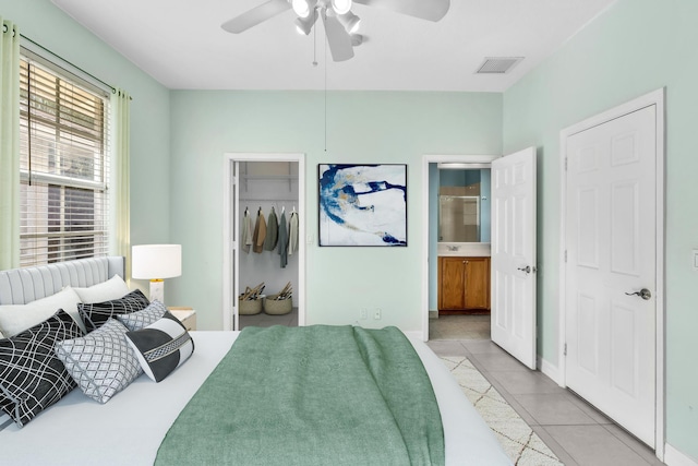 tiled bedroom featuring ensuite bathroom, a walk in closet, ceiling fan, and a closet