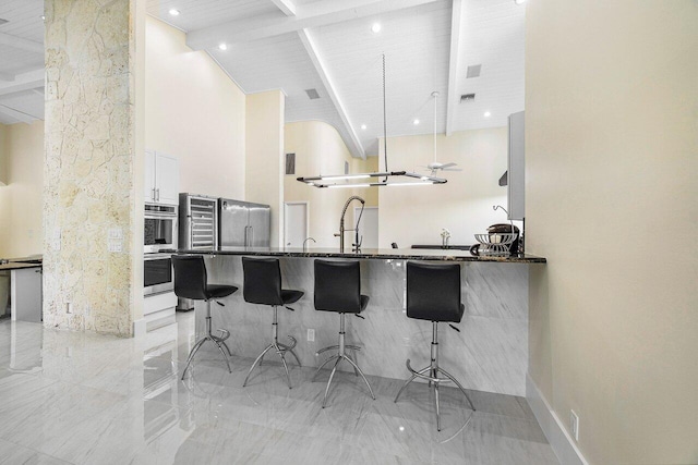 kitchen with white cabinets, beamed ceiling, kitchen peninsula, high vaulted ceiling, and a kitchen bar