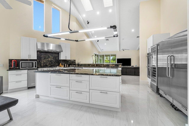 kitchen with white cabinets, stainless steel appliances, high vaulted ceiling, and wall chimney range hood