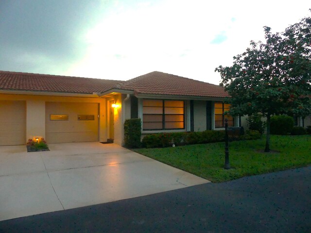 view of front of property featuring a garage, a tile roof, driveway, stucco siding, and a front lawn