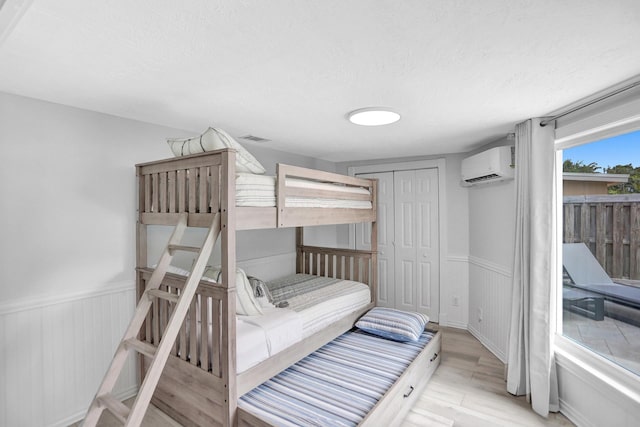 bedroom with a closet, light hardwood / wood-style flooring, and an AC wall unit