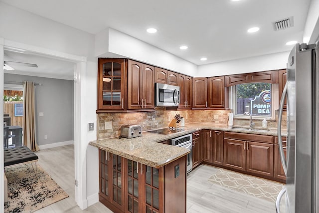 kitchen featuring tasteful backsplash, light wood-type flooring, sink, appliances with stainless steel finishes, and kitchen peninsula