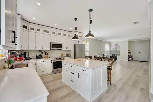 kitchen with stainless steel appliances, sink, backsplash, a kitchen island, and light wood-type flooring