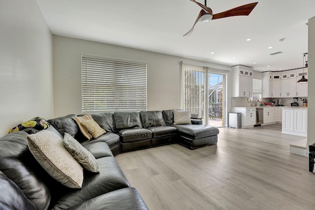 living room featuring sink, light wood-type flooring, and ceiling fan