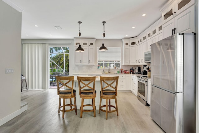 kitchen featuring appliances with stainless steel finishes, light hardwood / wood-style flooring, decorative light fixtures, decorative backsplash, and white cabinetry