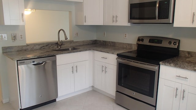 kitchen featuring appliances with stainless steel finishes, sink, white cabinets, and dark stone counters