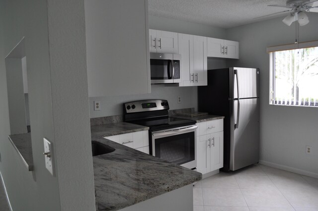 kitchen featuring ceiling fan, appliances with stainless steel finishes, white cabinets, light tile patterned flooring, and stone countertops