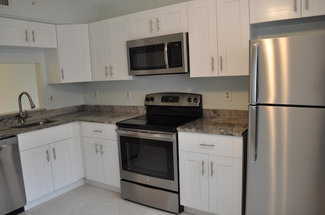 kitchen with dark stone countertops, light tile patterned floors, appliances with stainless steel finishes, sink, and white cabinetry