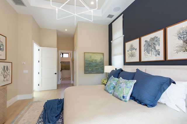 bedroom featuring light hardwood / wood-style floors, a notable chandelier, a towering ceiling, and ensuite bath