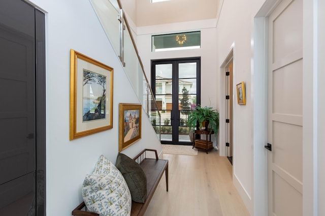 corridor with a high ceiling, light hardwood / wood-style flooring, and french doors