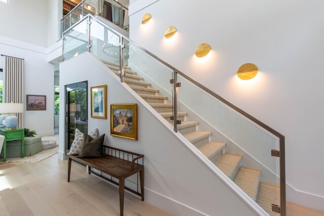 stairs with light wood-type flooring and a towering ceiling