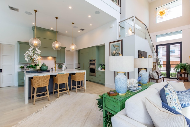 living room with french doors, light wood-type flooring, and a towering ceiling