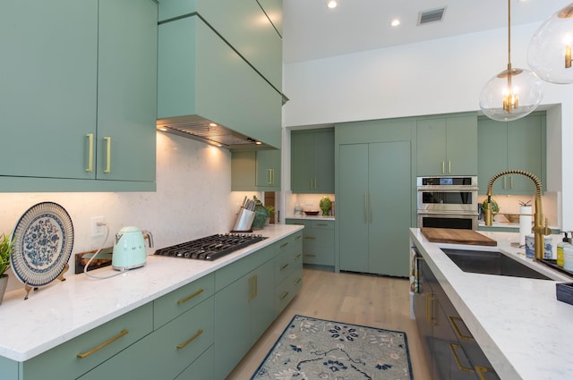 kitchen featuring green cabinets, sink, light stone counters, appliances with stainless steel finishes, and light hardwood / wood-style flooring