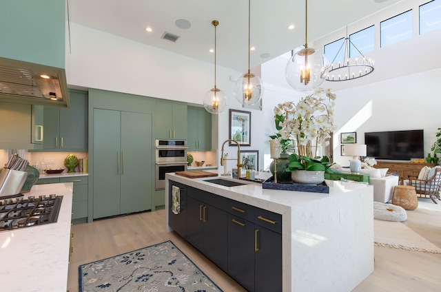 kitchen featuring appliances with stainless steel finishes, light hardwood / wood-style flooring, sink, light stone counters, and green cabinets