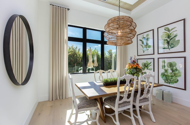 dining space with a raised ceiling, light hardwood / wood-style flooring, and a chandelier