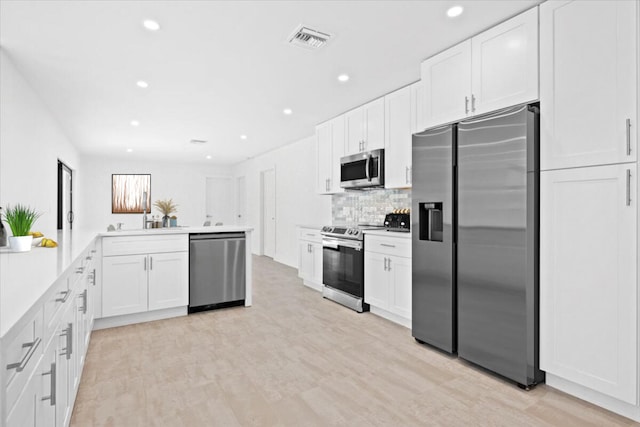 kitchen with kitchen peninsula, light wood-type flooring, white cabinetry, and stainless steel appliances