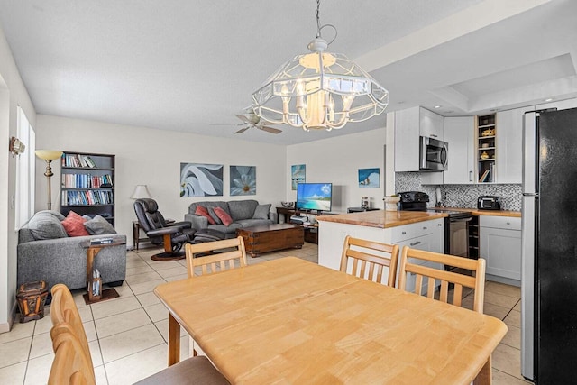 tiled dining space featuring ceiling fan with notable chandelier and a tray ceiling