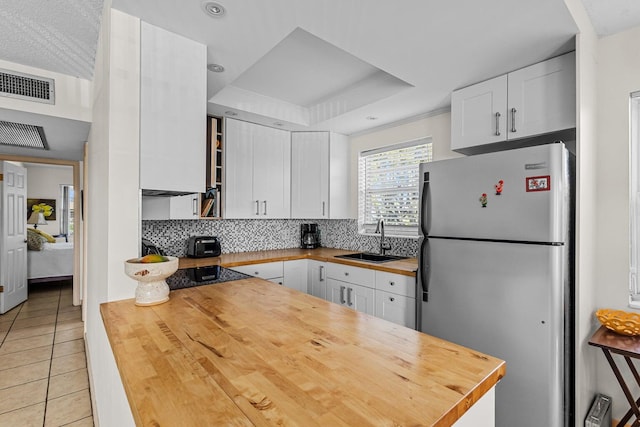 kitchen featuring white cabinets, stainless steel refrigerator, butcher block counters, decorative backsplash, and light tile patterned flooring