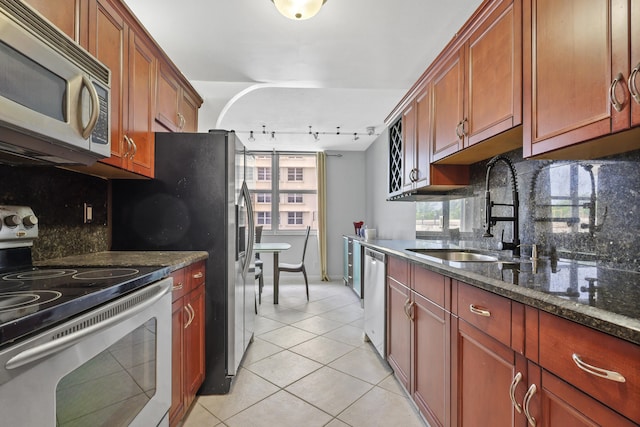 kitchen featuring dark stone countertops, light tile patterned floors, appliances with stainless steel finishes, backsplash, and rail lighting