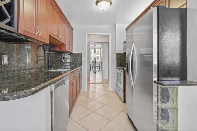 kitchen featuring appliances with stainless steel finishes, sink, backsplash, light tile patterned flooring, and dark stone counters