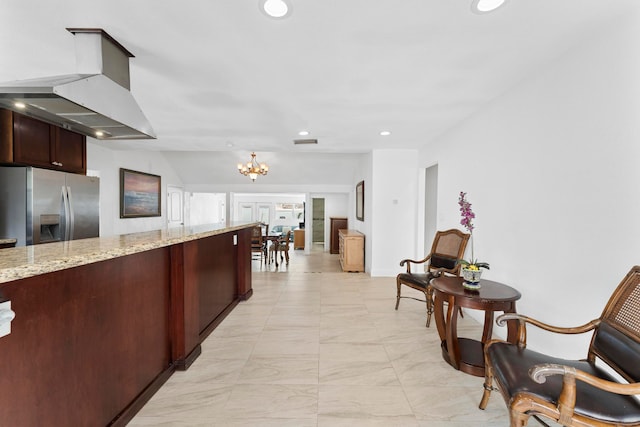 kitchen with stainless steel fridge with ice dispenser, wall chimney range hood, light stone countertops, a notable chandelier, and light tile patterned floors