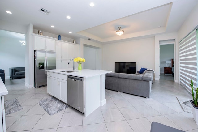 kitchen featuring a raised ceiling, stainless steel appliances, a kitchen island with sink, white cabinets, and sink